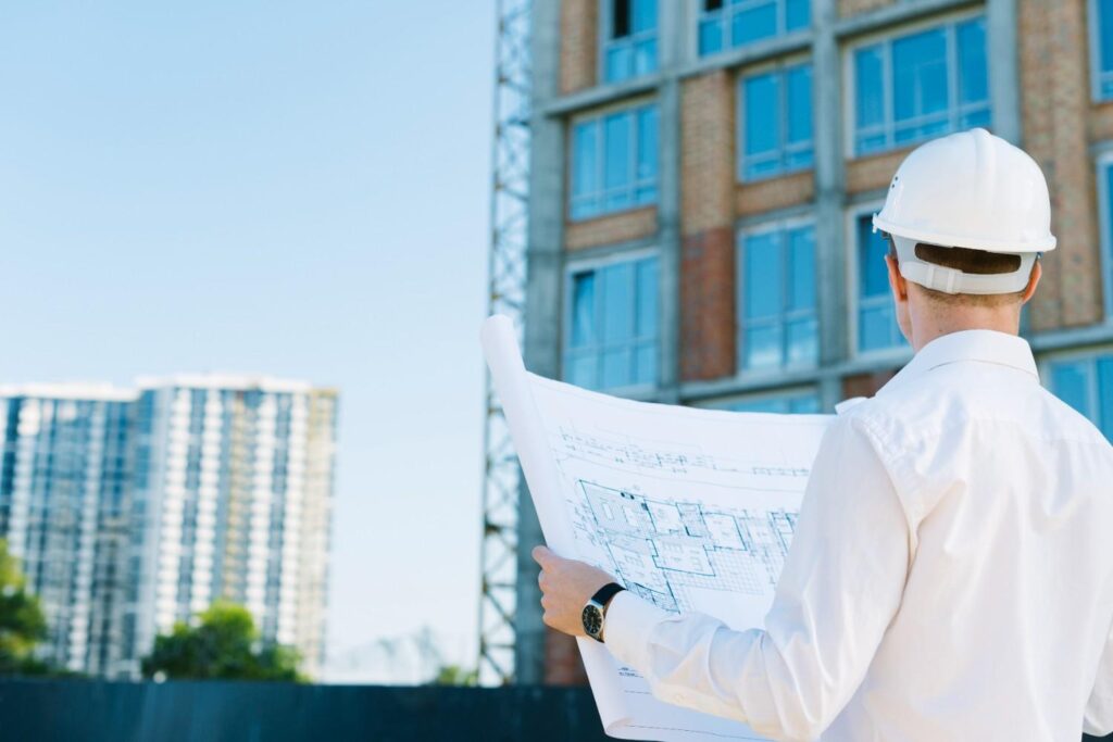 Engineer in a hard hat reviewing building blueprints on-site, illustrating key concepts in the Principles of Structural Engineering.